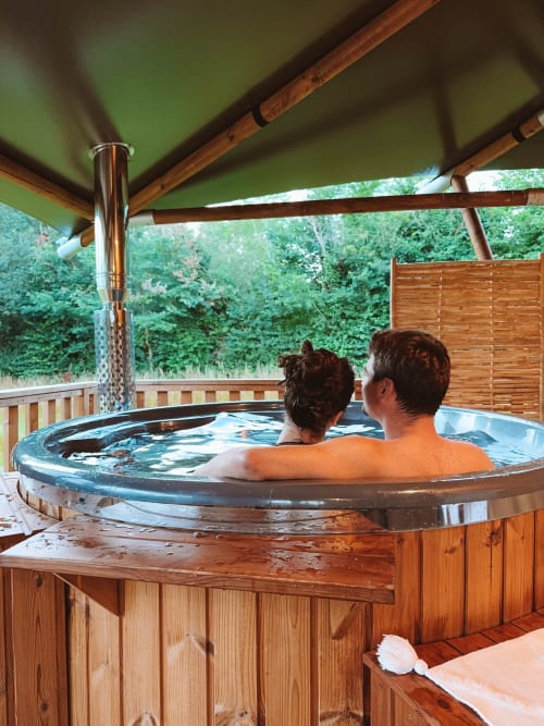 Two guests relaxing in a wooden hot tub under a green covered patio at You & Me Glamping in Moncontour, France