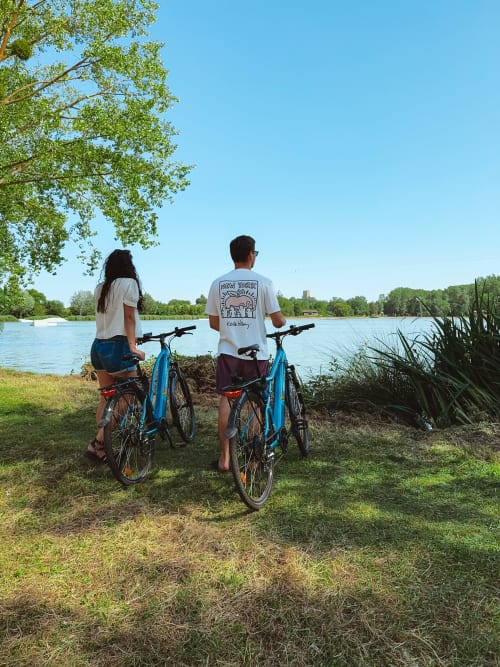 Two cyclists with blue bikes rest by a lake near Moncontour, France during glamping vacation