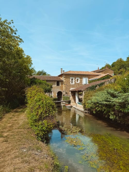 Rustic stone mill building with ivy along a waterway in Moncontour, France at You & Me Glamping