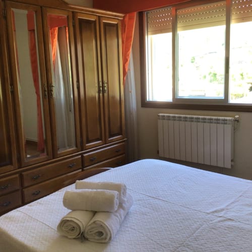 Dormitorio luminoso en la casa rural Houses by Pilar en Soutomaior con toallas blancas en la cama, armario de madera y vistas a la montaña