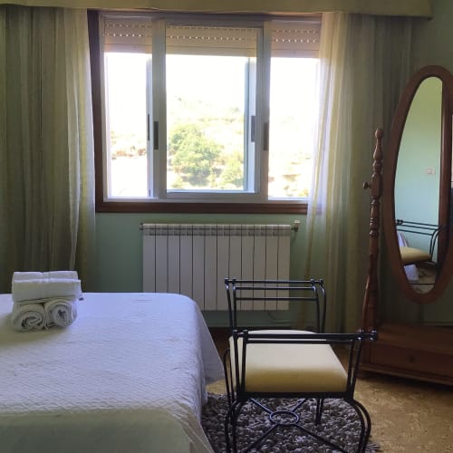 Dormitorio luminoso en la casita Houses by Pilar de Soutomaior con vistas a las montañas, cama blanca, espejo de madera y calefacción moderna