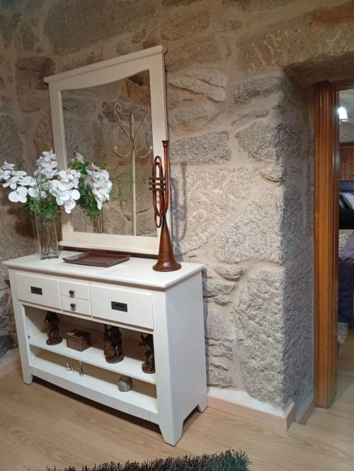 Cómoda blanca con espejo y artículos decorativos de madera contra pared de piedra rústica en la cabaña Houses by Pilar