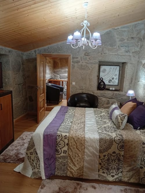 Dormitorio de la casita Houses by Pilar en Soutomaior con paredes de piedra, techo de madera y ropa de cama estampada