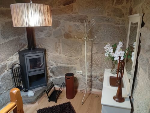 Interior rústico de cabaña de piedra en Houses by Pilar, Soutomaior con chimenea, lámpara y flores blancas