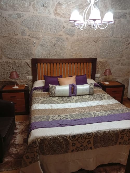 Elegante dormitorio en la cabaña Houses by Pilar con paredes de piedra, cabecero de madera, acentos púrpura e iluminación de candelabro