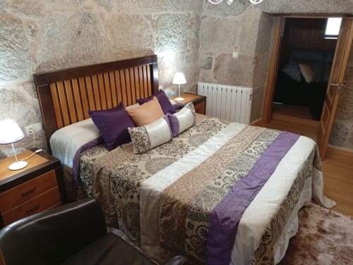 Elegante dormitorio en la casa rural Houses by Pilar en Soutomaior con muros de piedra, cama de madera y detalles en púrpura