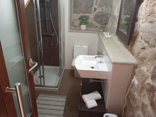 Baño moderno en la casa rural Houses by Pilar con ducha, lavabo rosa, inodoro y pared de piedra en Soutomaior
