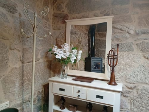 Tocador rústico de piedra con espejo blanco, flores decorativas y detalles en latón en Houses by Pilar, Soutomaior