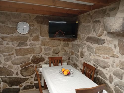 Comedor de casa de piedra con televisor, reloj, mesa de madera y sillas en Soutomaior
