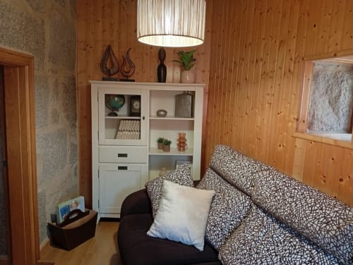 Acogedora habitación de cabaña con paredes de madera, sofá estampado, estanterías blancas y lámpara colgante en Houses by Pilar, Soutomaior