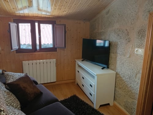 Acogedora sala de estar en Casas por Pilar con paredes de madera, TV en cómoda blanca, radiador y vistas a la montaña