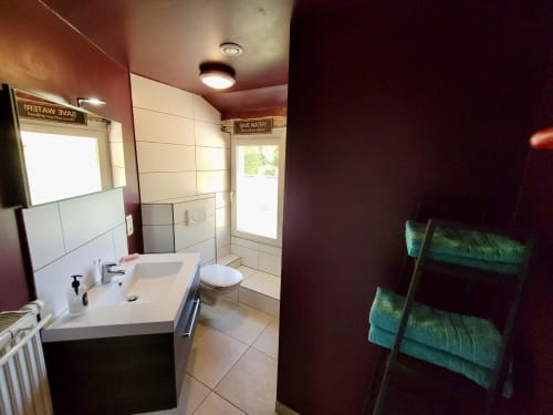 Salle de bain moderne du gîte Domaine de la Méouge avec carrelage blanc, lavabo, toilettes, douche, porte-serviettes et murs bordeaux