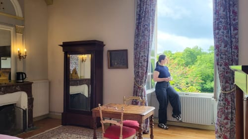 Femme à la Chambre des Marquis du Château de Gizeux, admirant les jardins luxuriants par les hautes fenêtres, décoration d'époque
