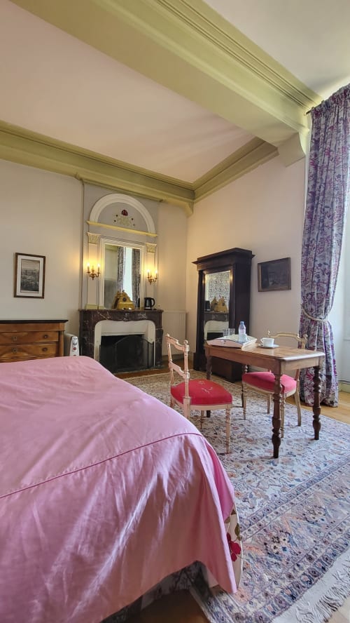 Chambre élégante du Château de Gizeux avec literie rose, cheminée et mobilier d'époque