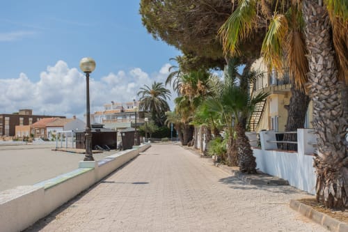 Paseo frente al mar en Haus Holiday Homes, Cartagena, con palmeras, playa de arena y arquitectura costera.