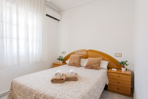 Dormitorio luminoso en Villa Hammely, Cartagena, con cama de madera, ropa de cama beige, toallas enrolladas, plantas en macetas y aire acondicionado split
