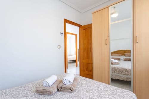 Dormitorio con toallas enrolladas sobre colcha estampada, puertas de madera, armario espejo, cabaña Villa Hammely en Cartagena