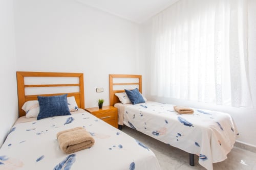 Dormitorio doble luminoso en Villa Hammely, Cartagena, con camas de madera, ropa de cama azul y cortinas translúcidas
