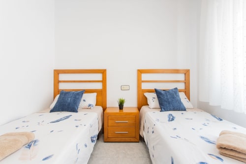 Camas gemelas con cabeceras de madera, almohadas azules y ropa de cama blanca con patrones de plumas en la cabaña Villa Hammely, Cartagena