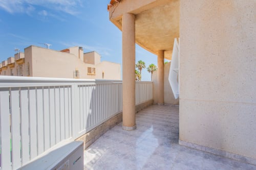 Soleada terraza de la casa Villa Hammely en Cartagena con barandillas blancas, columna de hormigón y palmeras al fondo