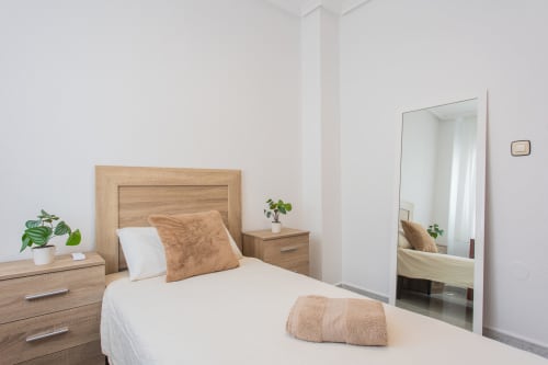 Dormitorio moderno en Villa Hammely de Cartagena con cama de madera, ropa blanca, detalles marrón y espejo de piso