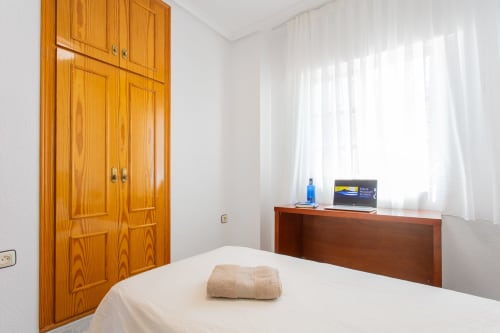 Dormitorio luminoso en Villa Hammely, Cartagena con armario de madera, escritorio con laptop, ropa de cama blanca y cortinas translúcidas