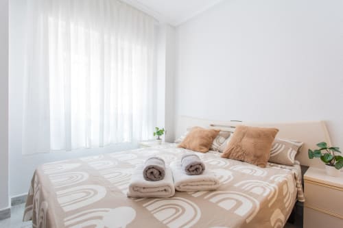 Dormitorio moderno y luminoso en Villa Hammely, Cartagena con ropa de cama de patrón geométrico beige, toallas enrolladas, almohadas decorativas