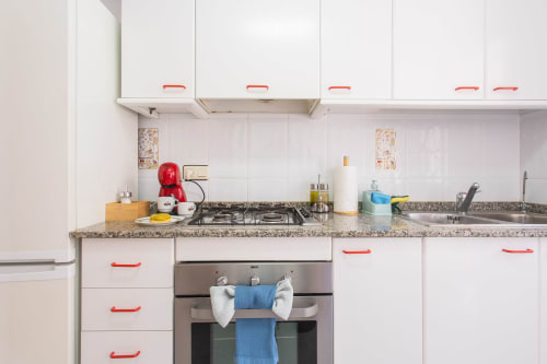 Cocina moderna con armarios blancos, encimera de granito, horno de acero inoxidable y manijas rojas en Villa Hammely