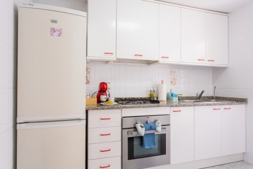 Cocina moderna blanca con tiraderas rojas, estufa a gas, horno integrado y refrigerador beige en la cabaña Villa Hammely, Cartagena.