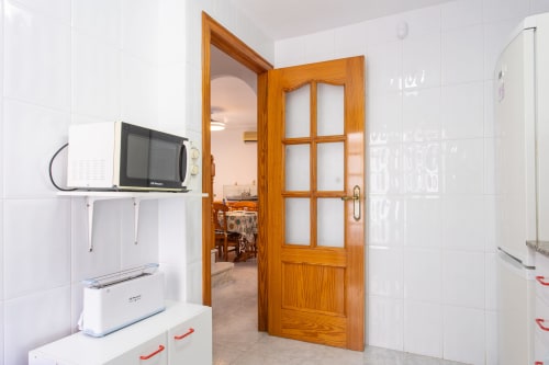 Cocina moderna en la villa Hammely de Cartagena con azulejos blancos, puerta de madera, microondas y acceso a baño compartido