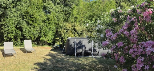 Garden view at Domaine en Terre Happy cottage in Labastide-de-Virac with loungers, purple flowers, and tree backdrop