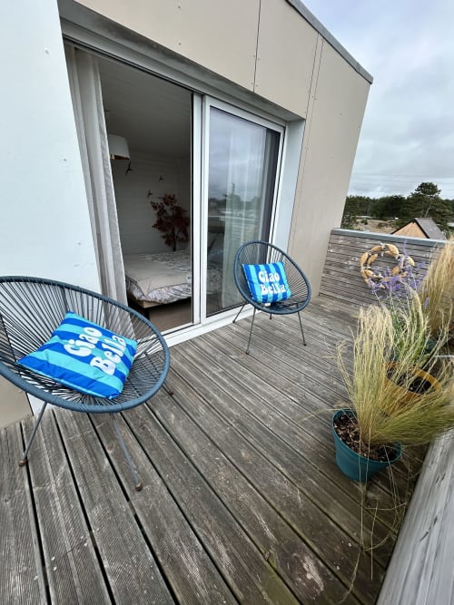 Coastal cottage deck with blue chairs, wooden terrace, and glass doors opening to bedroom at La Villa Plein Vent,
