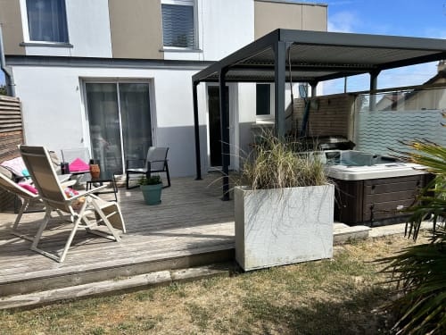 Backyard patio at La Villa Plein Vent cottage with deck, black pergola, hot tub, lounge chairs and garden view