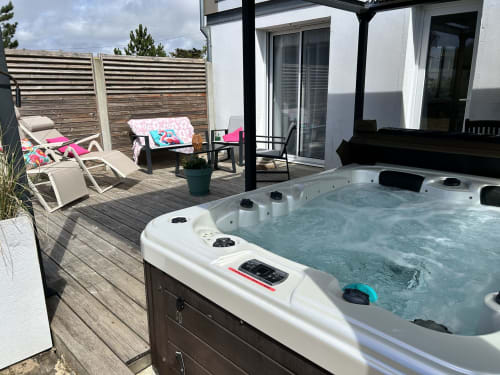 Jacuzzi on wooden deck with lounge chairs and striped fence at Le Skiff cottage, Barneville-Carteret