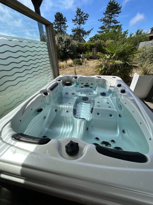 Empty hot tub on sunny deck at La Villa Plein Vent B&B in Barneville-Carteret, France with pine trees
