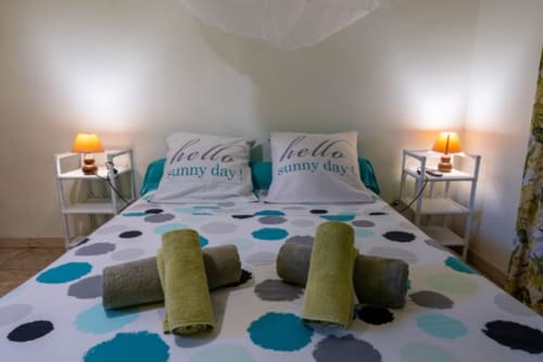 Chambre lumineuse aux Gîtes Bagatelle avec parure à pois, lampes doubles, coussins et serviettes décoratives à Sainte-Rose