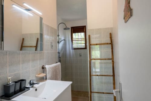 Salle de bain moderne avec douche à l'italienne, lavabo blanc et échelle à serviettes en bois aux Gîtes Bagatelle, Sainte-Rose