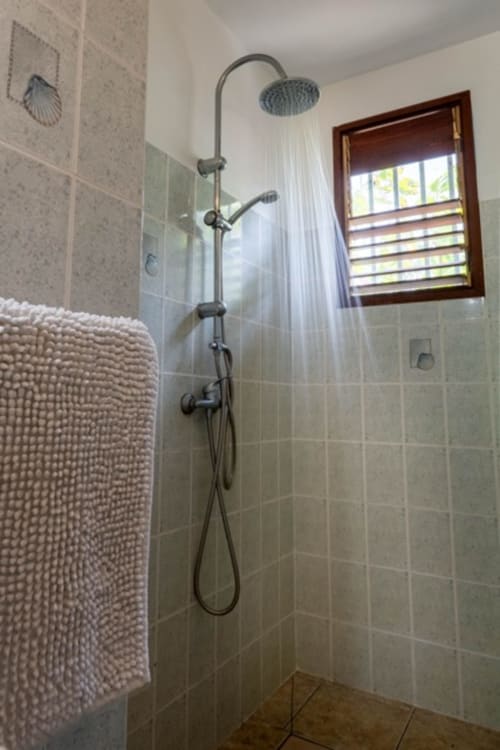 Salle de bain moderne aux Gîtes Bagatelle Sainte-Rose avec douche pluie, carrelage beige et volets en bois