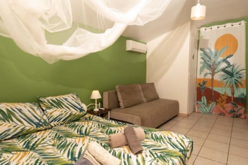 Chambre tropicale aux Gîtes Bagatelle, Sainte-Rose avec literie à motifs de feuilles de palmier, canapé marron et murs verts