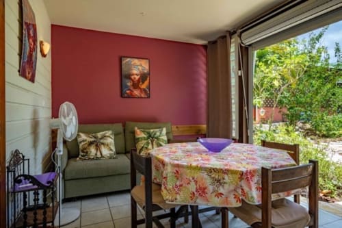 Chambre des Gîtes Bagatelle avec murs rouges, canapé vert, table fleurie et vue sur le jardin à Sainte-Rose