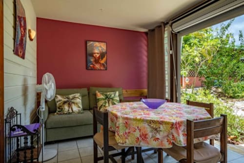 Studio confortable aux Gîtes Bagatelle à Sainte-Rose avec mur d'accent rouge, décor tropical et vue sur jardin