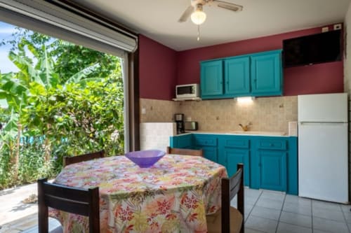 Cuisine et salle à manger lumineuses avec meubles turquoise, nappe fleurie et vue sur le jardin aux Gîtes Bagatelle, Sainte-Rose