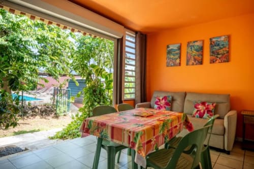 Intérieur orange vif aux Gîtes Bagatelle Sainte-Rose avec vue sur jardin tropical, mobilier coloré et accès à la terrasse