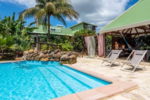 Espace piscine du Gîtes Bagatelle à Sainte-Rose avec transats, palmiers et bungalow à toiture verte