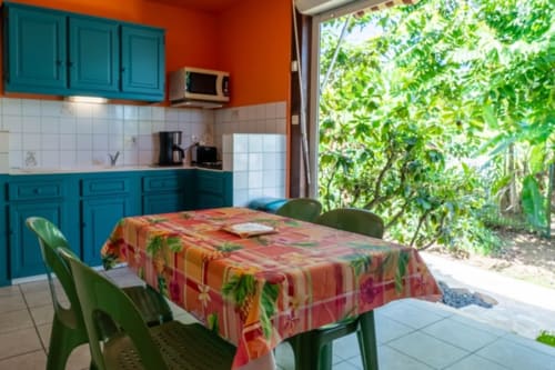 Bright kitchen and dining area in Guadeloupe cottage with turquoise cabinets, tropical garden view, and furnished table