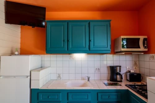 Bright kitchen with turquoise cabinets, orange walls, and white tile backsplash at Gîtes Bagatelle cottage in Guadeloupe