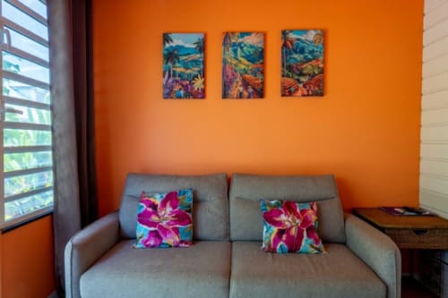 Bright orange living room with gray sofa, colorful floral pillows, and tropical artwork at Gîtes Bagatelle in Guadeloupe