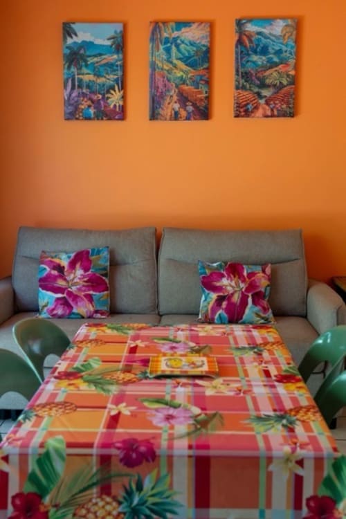Colorful cottage interior in Guadeloupe with vibrant orange walls, tropical pillows, and floral tablecloth at Gîtes Bagatelle
