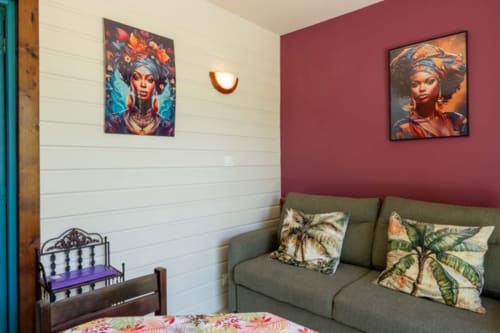 Colorful cottage bedroom at Gîtes Bagatelle with burgundy accent wall, vibrant artwork, green sofa with tropical pillows, and