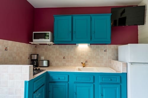 Bright turquoise kitchen with white appliances, beige tile backsplash, and pink walls at Gîtes Bagatelle in Guadeloupe